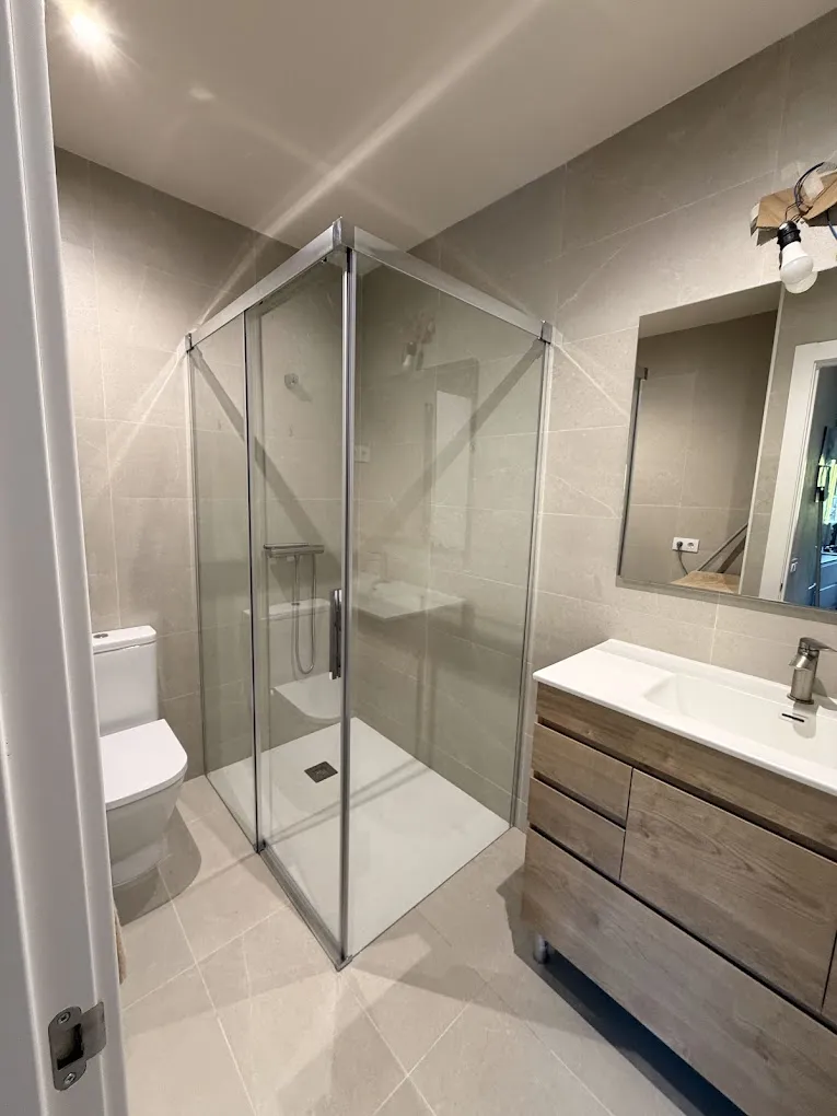 Baño con plato de ducha y mampara de cristal, mueble de lavabo de madera y espejo