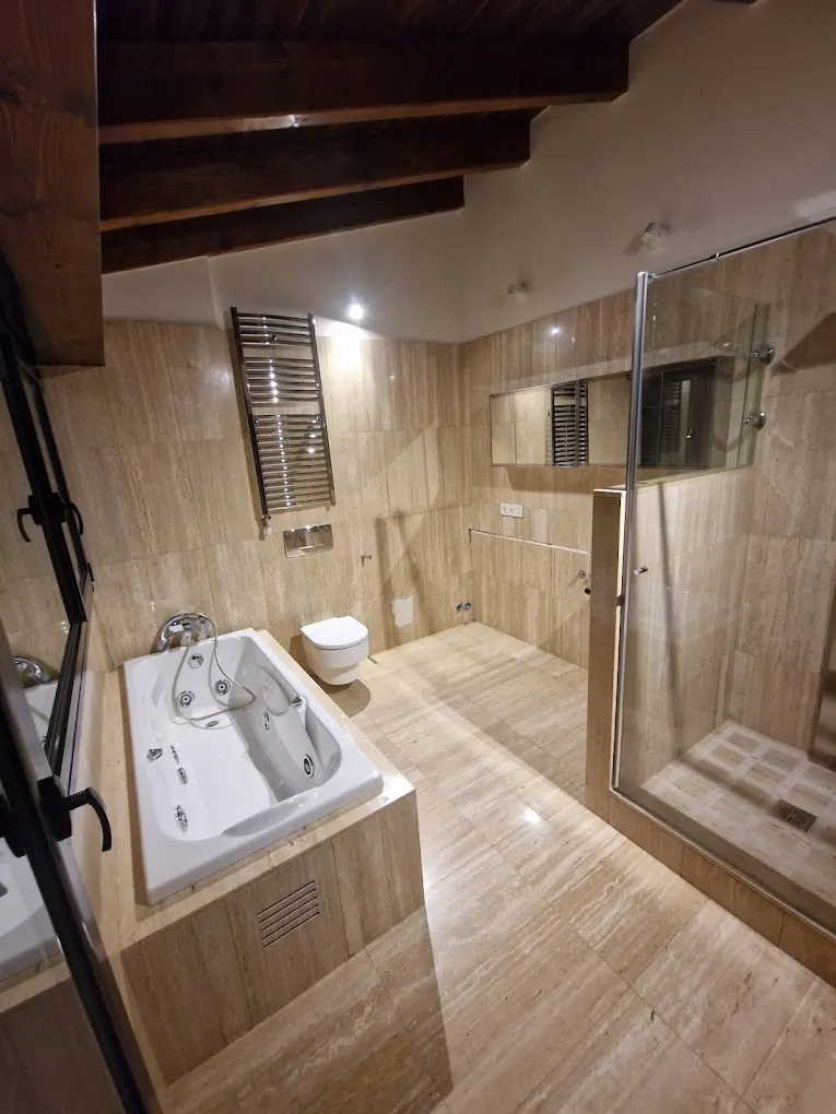 Baño revestido de piedra con bañera de hidromasaje, ducha de obra y vigas de madera en el techo