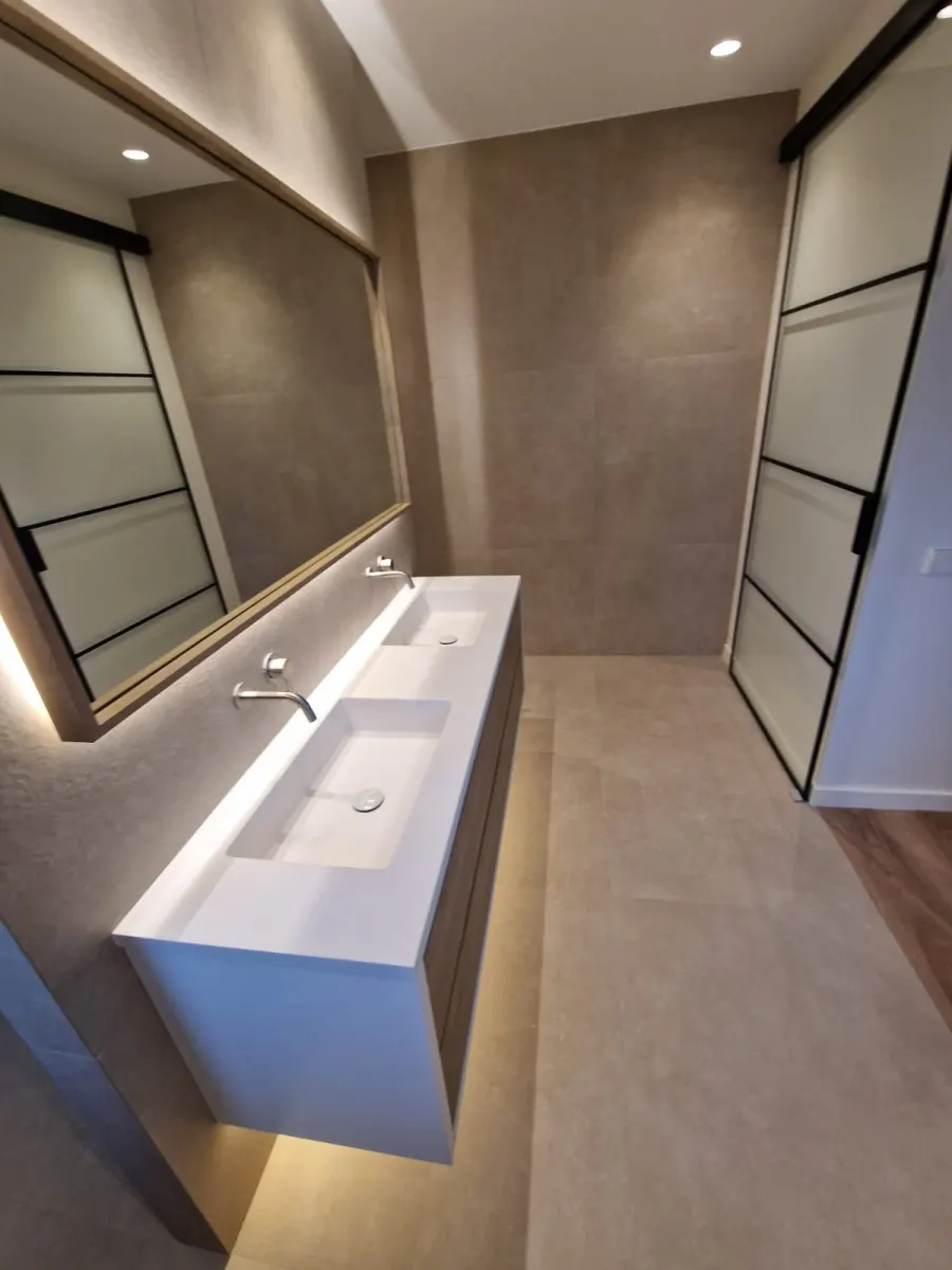 Baño reformado con lavabo doble, espejo grande con luz y mampara de cristal