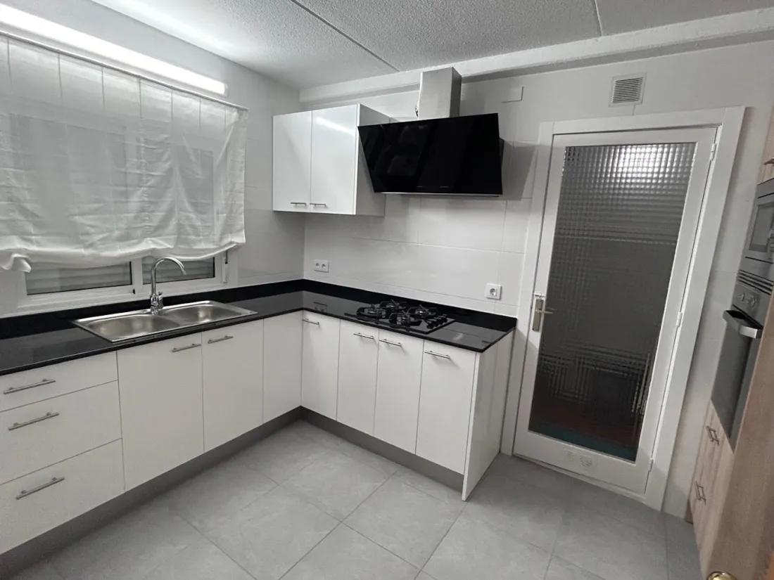 Cocina con muebles blancos, encimera negra y campana negra