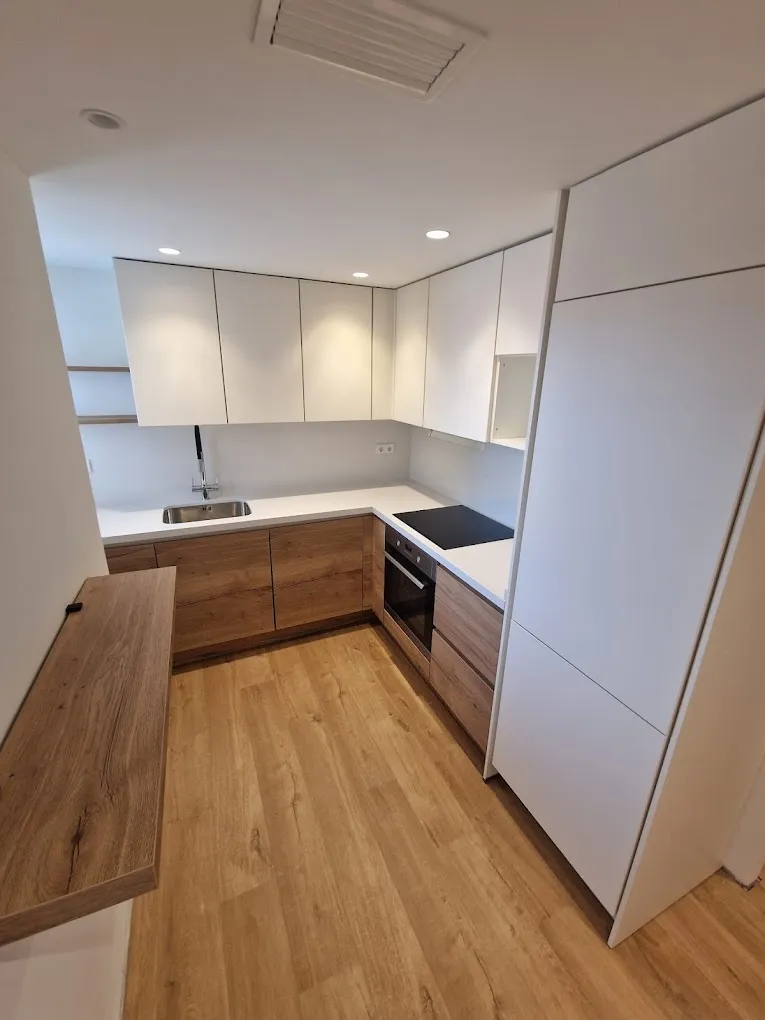 Cocina terminada con muebles blancos y de madera, encimera blanca y suelo de madera