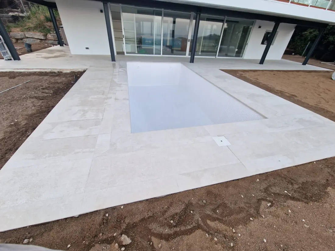 Piscina y terraza con pavimento claro junto a una casa